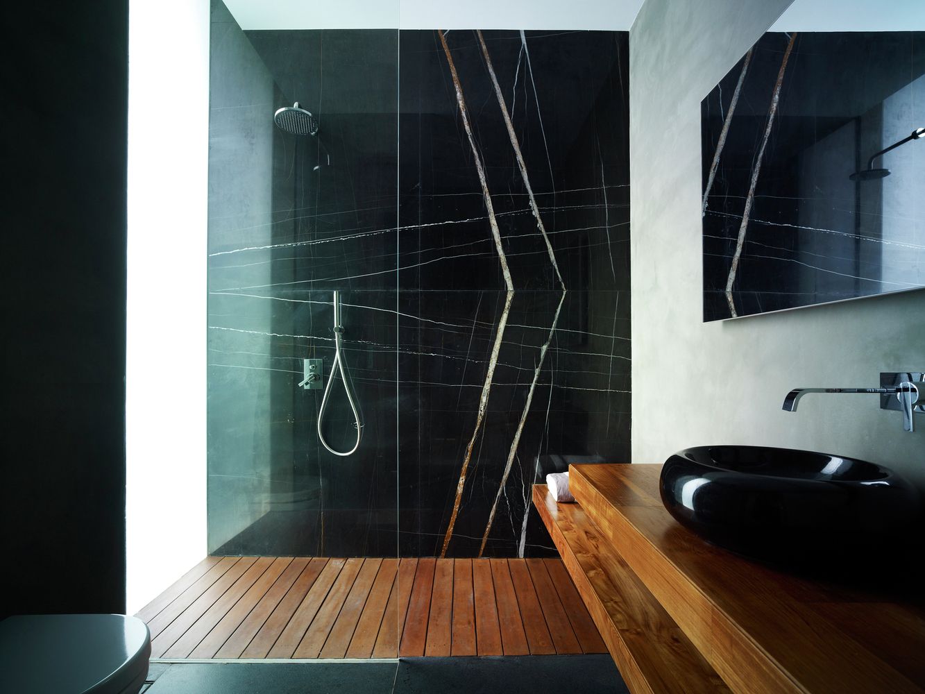 Shower with a large black marble wall and wood floor